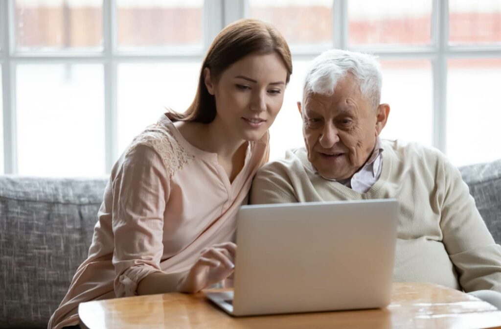 Young woman and elderly man looking at a laptop together, exploring memory care options.