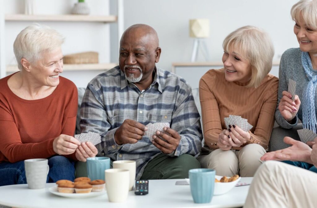 Group of seniors smiling and playing cards at a table with drinks and snacks