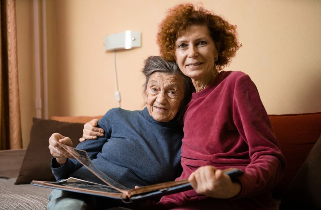 An adult and their older parent sit in an embrace while flipping through a photo album during a memory care visit