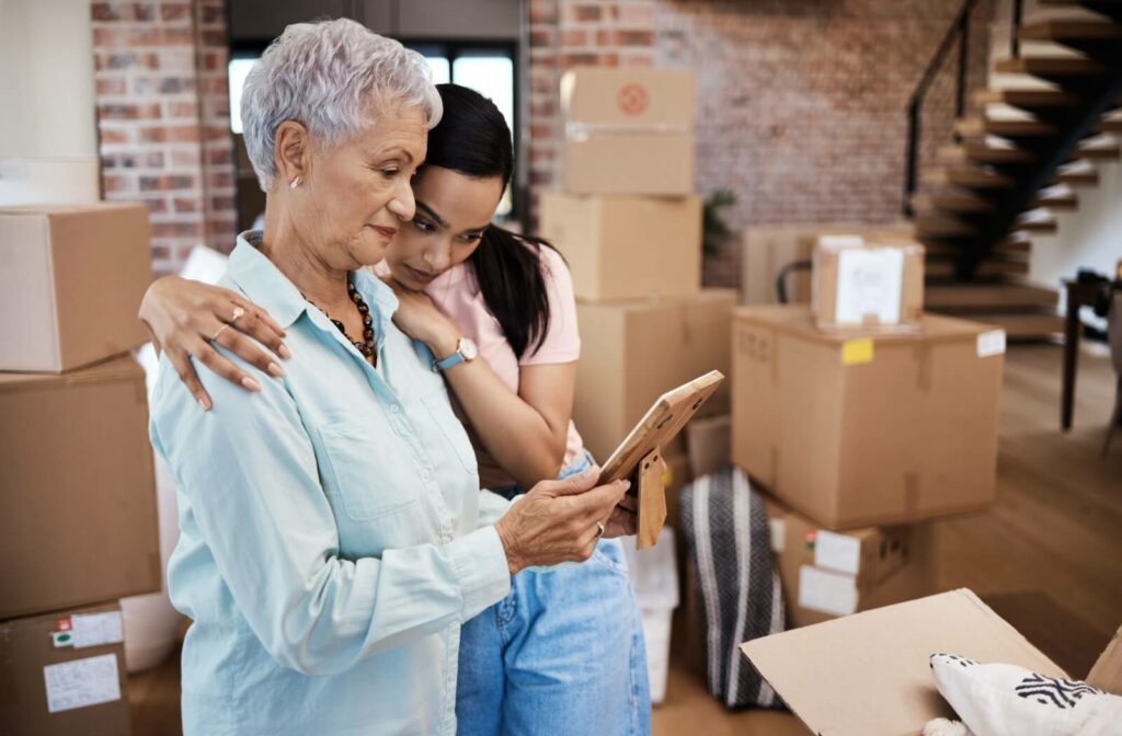 A senior is looking at a photograph with their adult child while packing boxes on moving day to a senior living community.