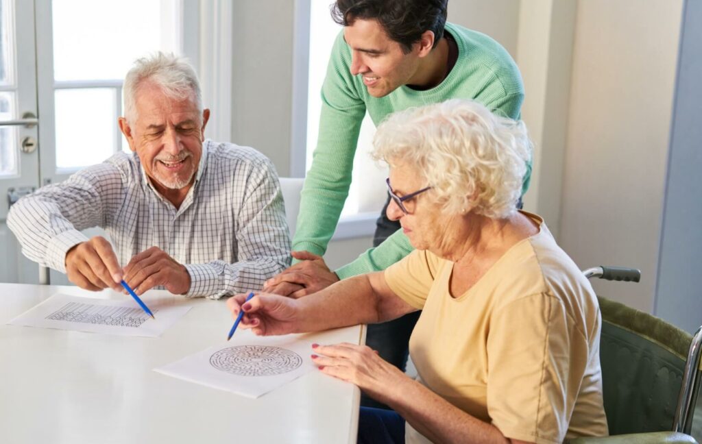 A staff member helps two seniors solve a puzzle as a therapeutic activity to help preserve cognitive function.
