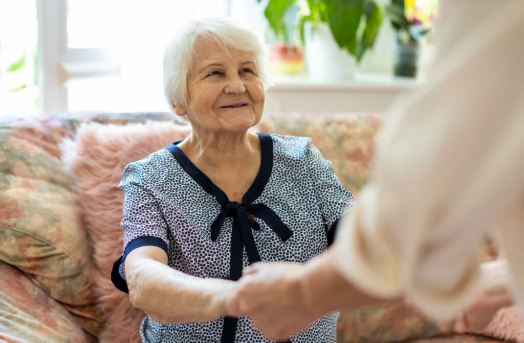 a senior woman sitting on sofa getting help to stand up in assisted living