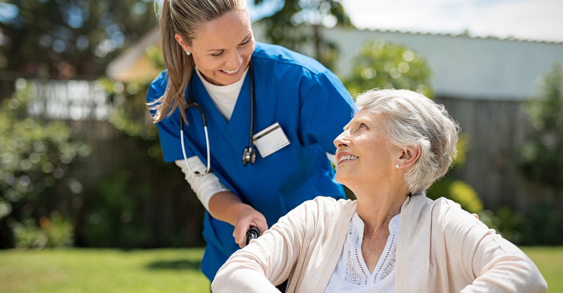 caretaker walking a woman in a wheelchair outside while smiling together