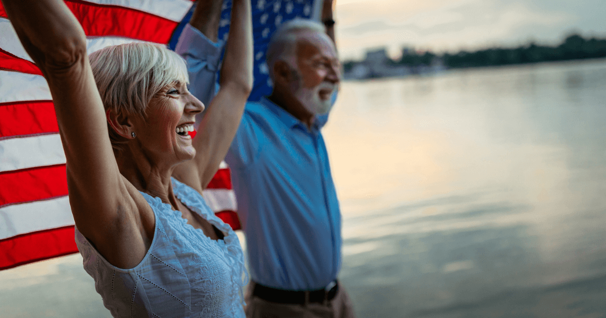 Older couple holding an American flag up behind their backs.