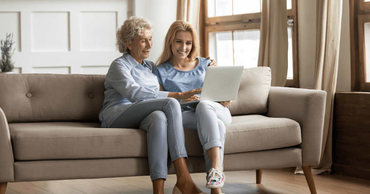 Senior woman and adult daughter sitting on the sofa comparing the cost of senior living.