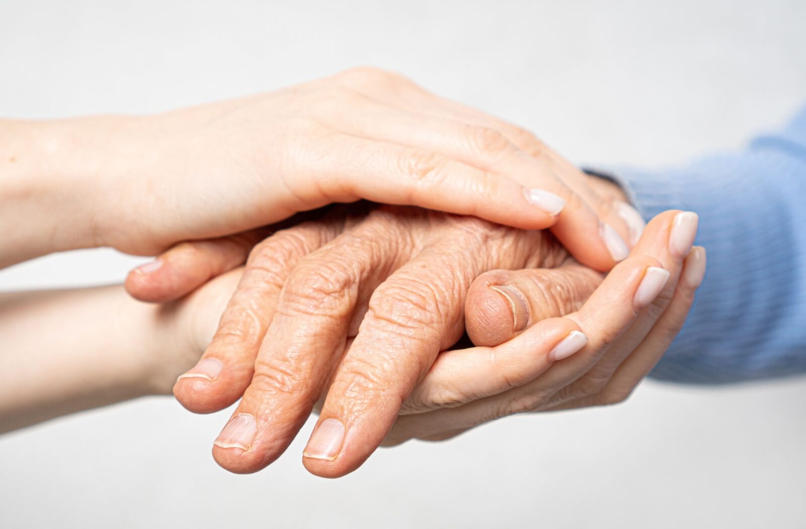 Close-up of a younger person gently holding the hands of an older adult, symbolizing compassion, care, and support in a memory care or assisted living setting.