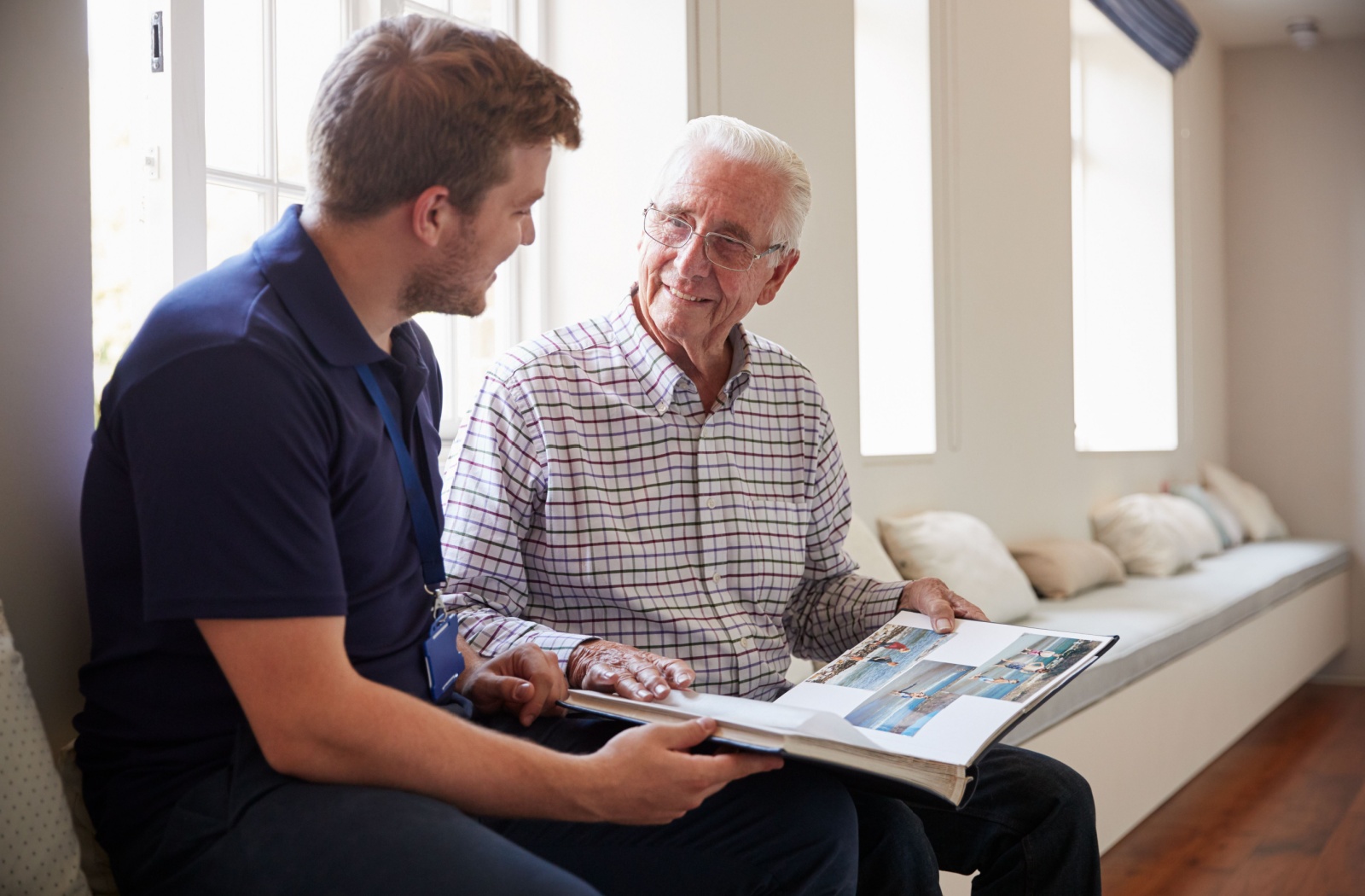 A senior with dementia sits looking at a photo album with their adult child, recounting memories.