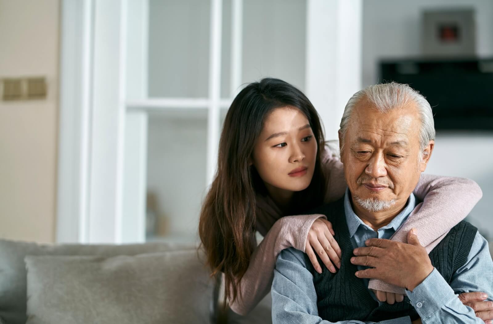 A worried young adult wraps their arms around their grandparent’s shoulders following an Alzheimer’s diagnosis
