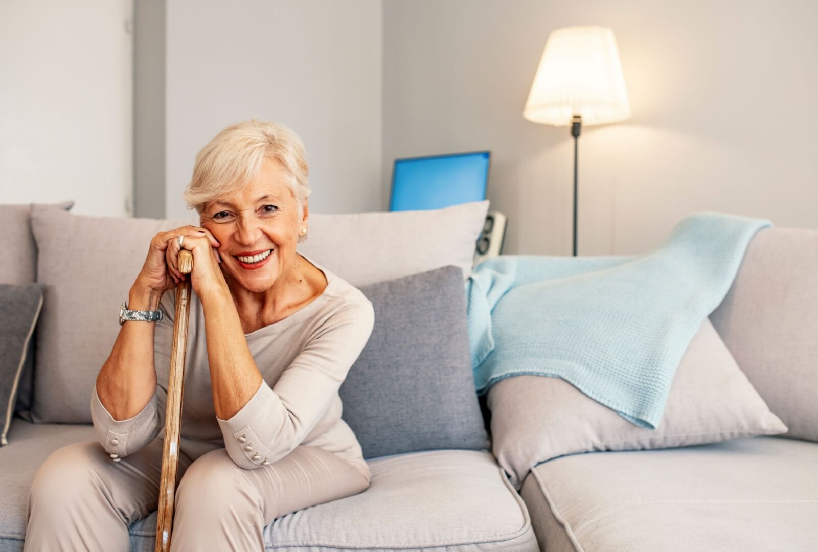 Senior sitting on a sofa holding a cane and smiling in a senior living community.